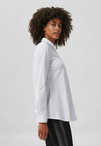 Witte langmelding shirt met een kraag, knoopdetails aan de voorkant en opgerolde manchetten; gladde, lichte stof met een gestructureerde pasvorm.