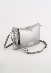Srebrna, wyściełana torebka na ramię o błyszczącej fakturze, z zamkiem błyskawicznym i kolorowym pomponem. Posiada odpinany szary pasek.