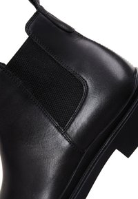 Stivale in pelle nera ankle con un pannello laterale elasticizzato texturizzato, design elegante e suola robusta con un leggero tacco.