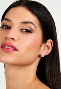 Orecchini a bottone rotondi con un centro in pietra preziosa rosa circondato da piccole pietre chiare, montati su una base metallica.