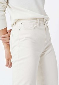 Jeans de tiro alto, de color beige claro, confeccionados en denim con una textura suave, que cuentan con bolsillos laterales y detalles de costura mínimos.