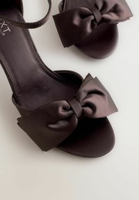 Zwarte satijnen sandalen met een brede strikaccent aan de voorkant, open teen ontwerp en een dunne enkelband. Glad textuur en ronde vorm.