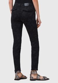 Pantalones cargo negros con un patrón de camuflaje, que presentan un diseño ajustado y bolsillos con parche. Combinados con sandalias metálicas de tiras.