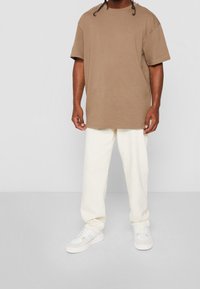 Hnědé oversized tričko vyrobené z bavlny, doplněné krémovými kalhotami a bílými teniskami. Jednoduchý design, krátké rukávy, uvolněný střih.