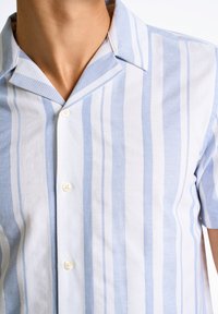Camicia a maniche corte azzurro chiaro e bianca a righe, con colletto ad alette, caratterizzata da una parte anteriore con bottoni e una morbida texture in cotone.