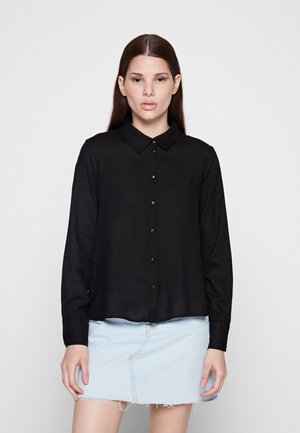 Camicia nera a maniche lunghe con colletto button-down, caratterizzata da una consistenza liscia e una leggera lucentezza, abbinata a una gonna in denim chiaro.