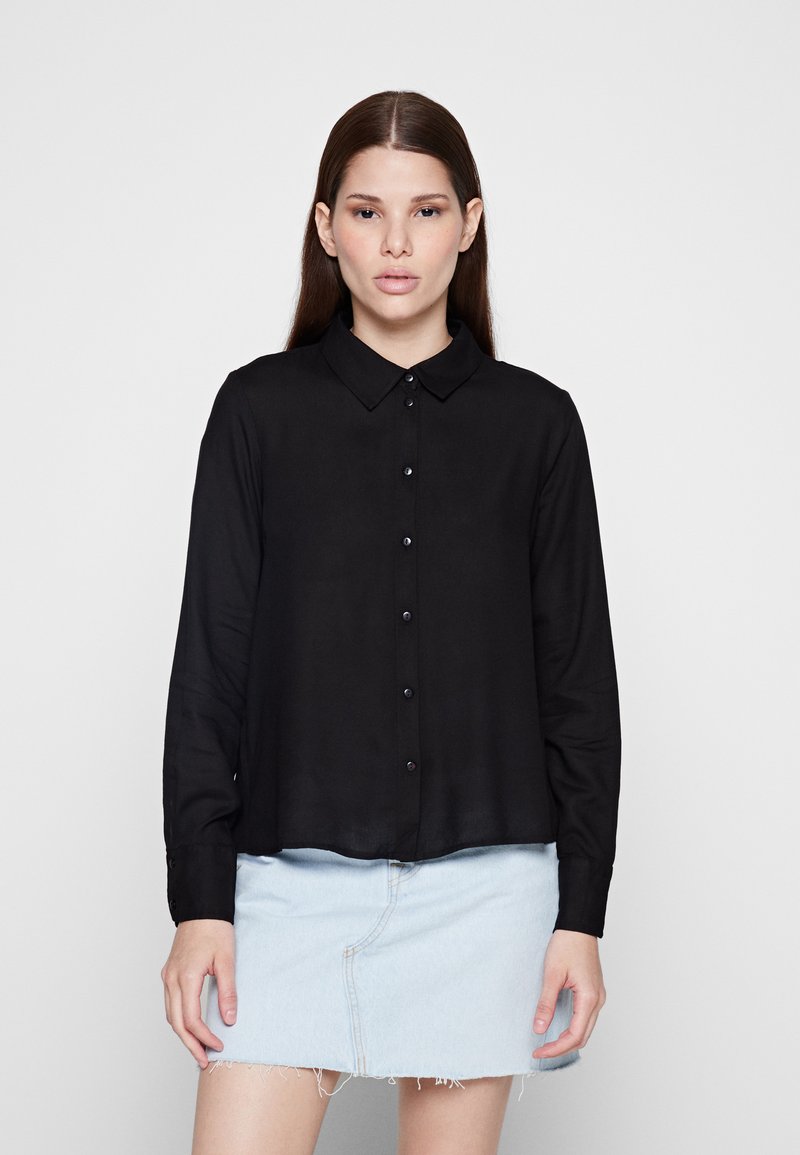 Must mustriga pikkade varrukatega särk, millel on nööbid all ja sile tekstuur ning peen sära, koos heleda denimminekaga.