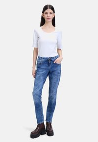 Witte short-sleeve top gecombineerd met lichtblauwe jeans. De jeans hebben een smalle pasvorm en een versleten uitstraling. Bruine platformlaarzen maken de outfit af.