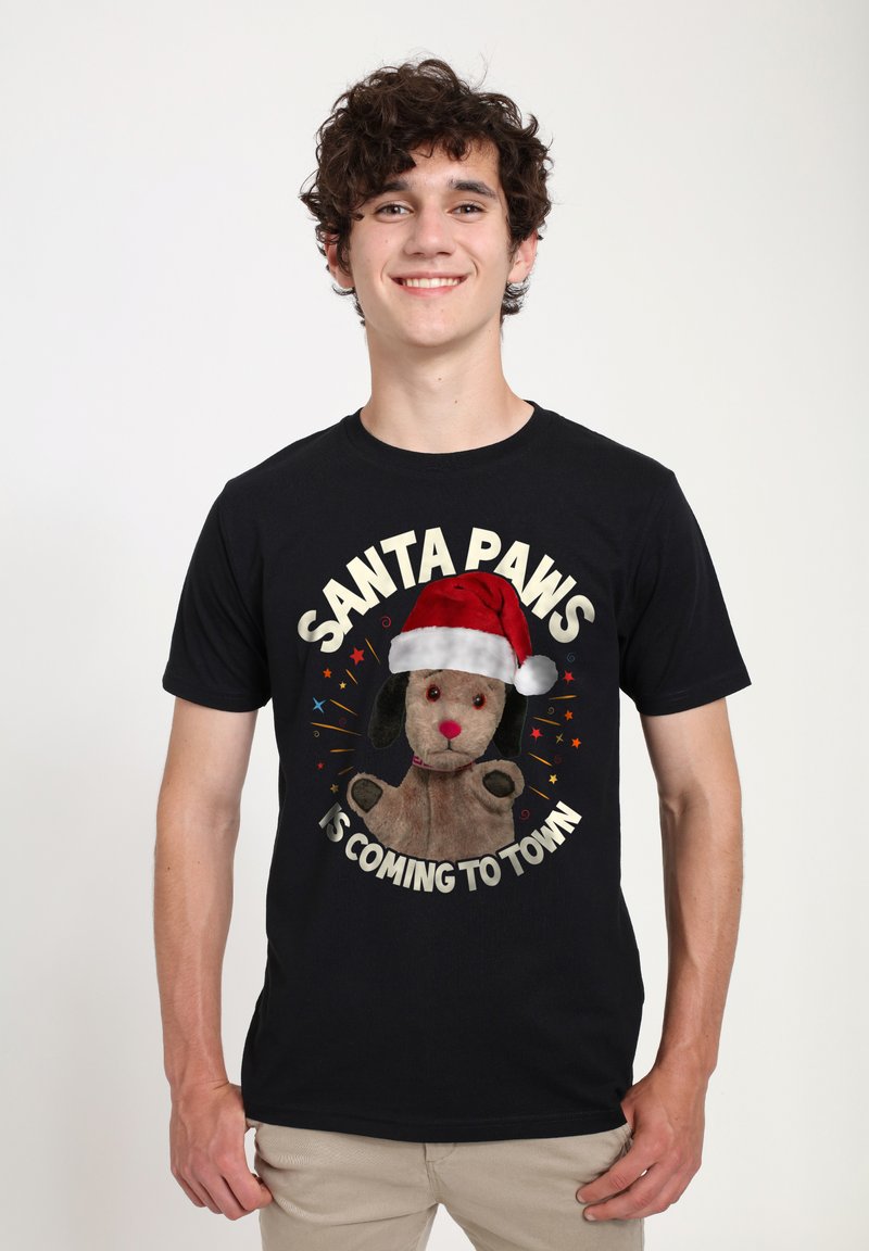Svart t-shirt med ett motiv av en plyschhund som bär en röd tomteluva, med texten "SANTA PAWS ÄR PÅ VÄG TILL STAN" i vitt.