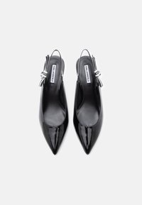 Zapatos de charol negro con tira trasera y punta afilada, que cuentan con una correa decorativa en el tobillo y detalle de logo. Textura suave, diseño elegante.