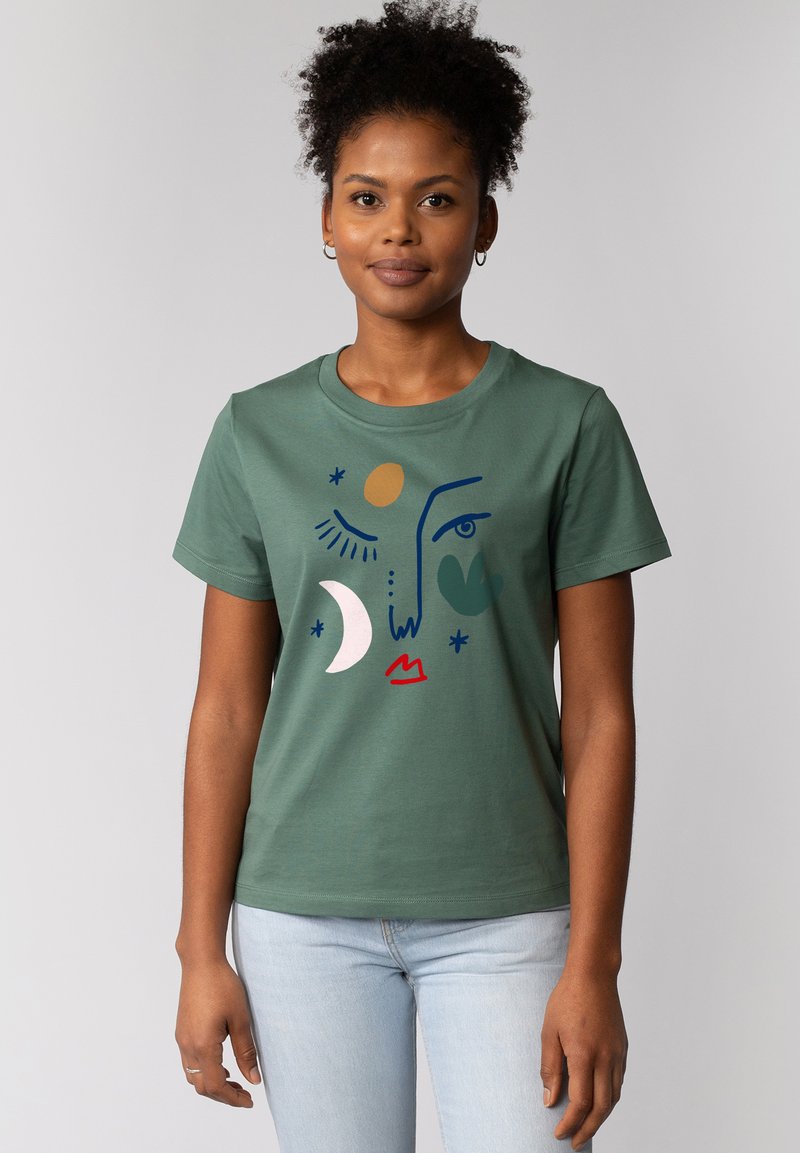 T-shirt en coton vert avec un imprimé artistique de la lune, du soleil et d'un visage abstrait en bleu, rose et rouge. Encolure ras du cou simple et manches courtes.