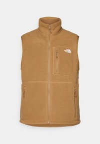 Kamizelka z polarowego materiału w kolorze tan, z wysokim kołnierzem, przednim zamkiem i dwoma bocznymi kieszeniami. Posiada kieszeń na klatce piersiowej oraz logo po lewej stronie. Miękka w dotyku.