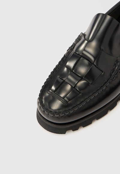 Μαύρο δερμάτινο μοκασίνι με υφαντή λεπτομέρεια στην επάνω πλευρά, ανασηκωμένο γιακά και παχύ, υφασμένο πέλμα.