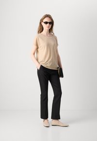 Beige T-shirt met korte mouwen, zwarte op maat gemaakte broek en beige platte schoenen. Accessoires zijn onder andere een zwarte clutch en zwarte ovale zonnebril.