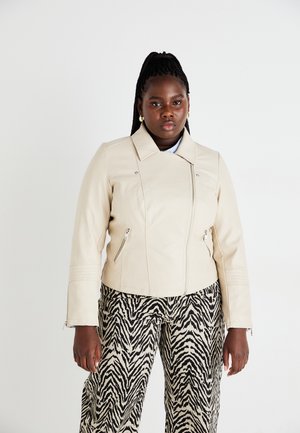 Veste de moto en cuir beige avec des zips sur les côtés et un col haut, associée à un pantalon à motif zèbre noir et blanc.