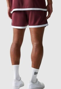 Bermudas atléticas en color burdeos con ribetes blancos, tejido texturizado y un ajuste suelto; combinadas con zapatillas blancas y calcetines de longitud media.