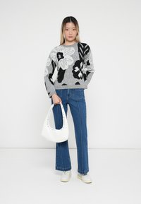 Maglione grigio con motivo floreale in bianco e nero, abbinato a pantaloni flare in denim blu. Borsa bianca con dettagli a borchie e sneakers bianche.
