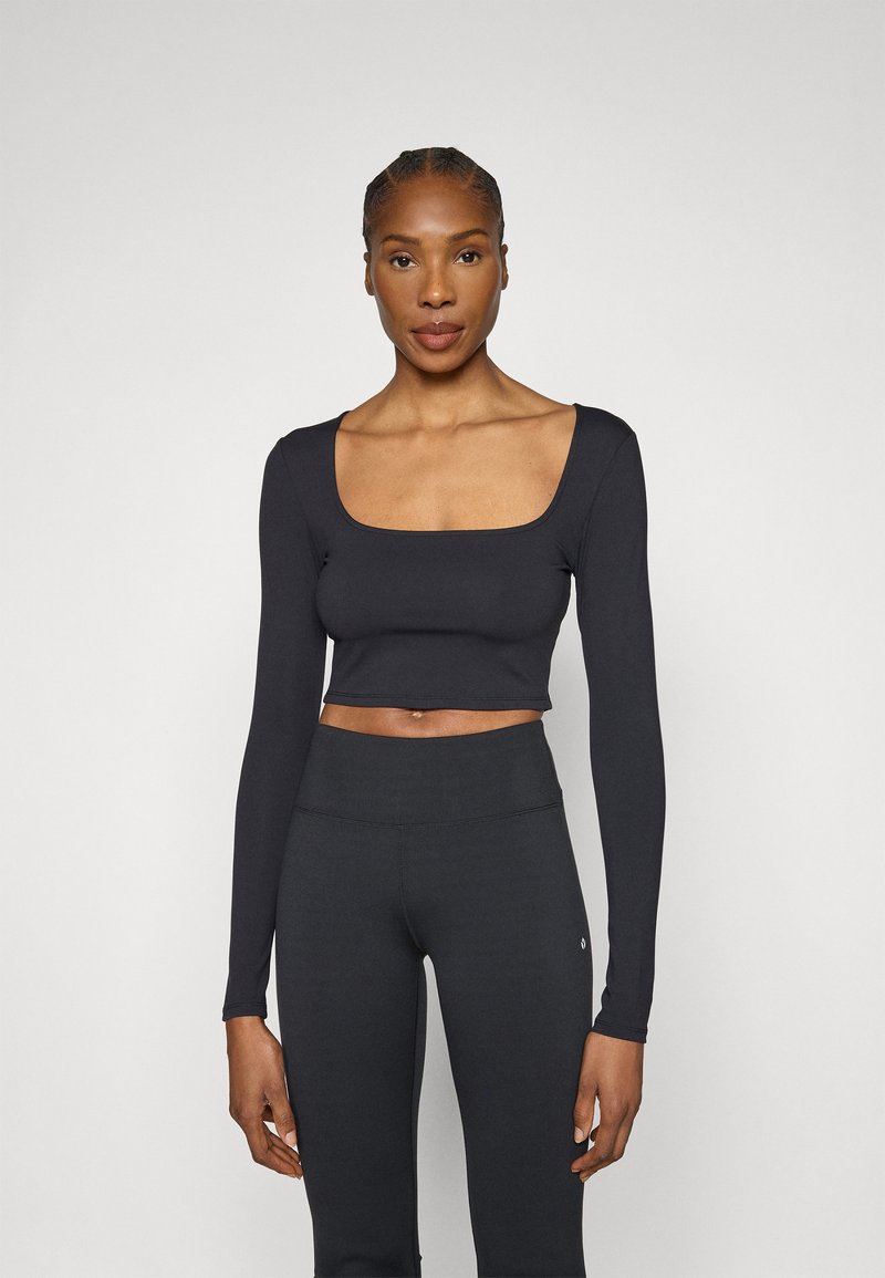 Čierny crop top s dlhým rukávom a štvorcovým výstrihom, vyrobený z hladkej látky. Kombinovaný s vysokým pásom čiernych legín. Minimalistický dizajn.