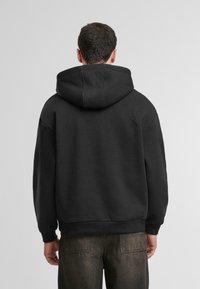 Sudadera negra de gran tamaño con una capucha grande, puños y dobladillo acanalados. La tela parece suave y tiene un diseño simple y limpio, vista desde la parte posterior.