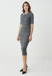 Robe en tricot à manches courtes, rayures bleu marine et argent, silhouette ajustée, longueur genou et col. Associée à des escarpins noirs à bout pointu.