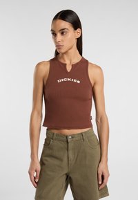Hnědý žebrovaný crop top s kulatým výstřihem a malým výřezem uprostřed, s bílým nápisem "DICKIES" přes hrudník.