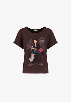 Maglietta marrone scuro con la grafica di una donna seduta, che tiene un caffè, indossa jeans, sneakers e una borsa rossa, con il testo "Just me and my coffee".