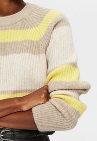 Strickpullover mit abwechselnden Streifen in hellem Beige, Braun und leuchtendem Gelb; gerippte Textur; breite Bündchen; runder Halsausschnitt.