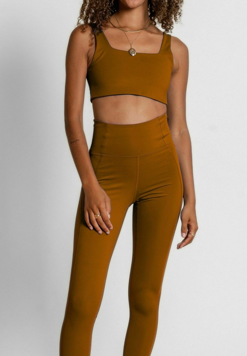 Top corto marrón y leggings de cintura alta hechos de material elástico. El top presenta un escote cuadrado, y los leggings tienen un acabado suave.