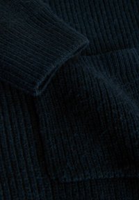 Material tricotat albastru închis, cu textură moale, prezentând manșete pliate și o cusătură centrală, sugerând un articol vestimentar cald și confortabil.