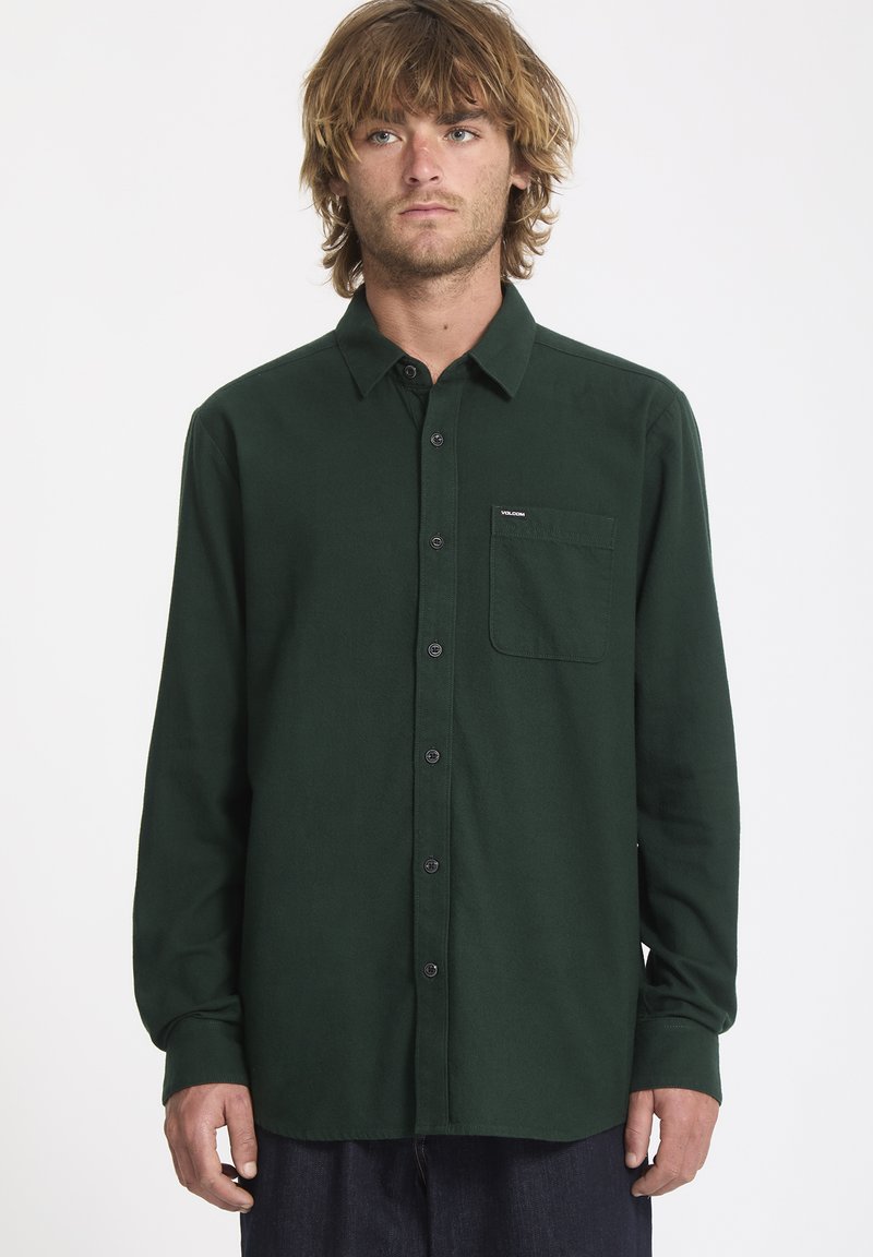Chemise verte à manches longues en tissu doux, dotée d'une fermeture à boutons sur le devant, d'un col et d'une poche sur la poitrine gauche avec un patch logo.