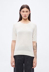 Kremna kratka pletena majica z okroglim izrezom in rebrastim robom, združena s temnimi širokimi hlačami. Mehak otip, lahkotno blago.