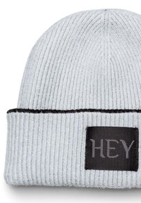 Grijze geribde beanie met een zwarte horizontale accentband. Heeft een vierkante patch met de tekst "HEY" in grijze letters op een zwarte achtergrond.