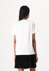 Tricou alb din bumbac, cu mâneci scurte, decolteu rotund și tiv drept. Pur tat cu o fustă plisată neagră, cu un material texturat.
