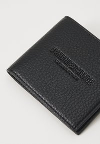 Portafoglio in pelle nera con superficie texturizzata. Presenta il logo "ARMANI EXCHANGE" impresso. Design compatto con struttura a bifold.