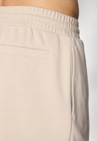 Hellbeige Sweatpants mit elastischem Bund, seitlichen Taschen und glatter Textur. Verfügt über eine Gesäßtasche mit einem kleinen Schlitzöffnungs.