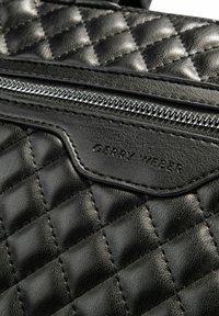 Borsa in pelle nera trapuntata con zip argentata e nome del brand impresso, superficie strutturata e linee pulite e angolari.