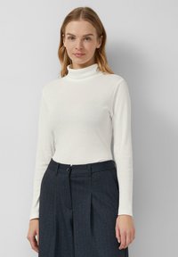 White turtleneck top with long sleeves, fitted design, made from smooth fabric; paired with navy pinstriped trousers featuring a front button.