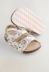 Witte sandalen met roze gespen, voorzien van een print van een cartoonfiguur. Textuur, gevoerd voetbed en een golvende roze rubberen zool.
