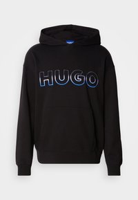 Svart hettegenser med kengurulomme, med bold "HUGO"-logo i reflekterende blå og sølvfarge på fronten. Myk tekstur, uformelt design.