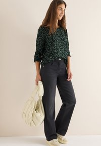 Maglietta a maniche lunghe con stampa leopardata verde abbinata a jeans neri a gamba larga e una borsa color crema. Gli accessori includono sneakers di colore chiaro.