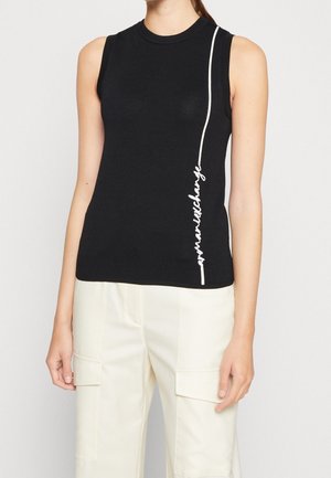 Hihaton musta toppi, jossa valkoista pystysuoraa tekstikuvaa oikealla sivulla, yhdistetty kermaan vivahtaviin cargo-housuihin, joissa läppätaskut.