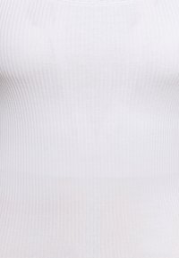 Vit ribbad linne gjort av stretchmaterial, med rund halsringning och en åtsittande silhuett med subtila vertikala linjer.