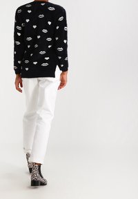 Black fuzzy sweater featuring white heart and lip patterns, paired with white jeans and black and white animal print ankle boots.
