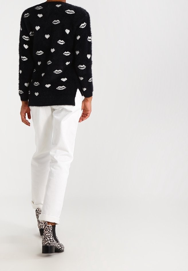 Black fuzzy sweater featuring white heart and lip patterns, paired with white jeans and black and white animal print ankle boots.