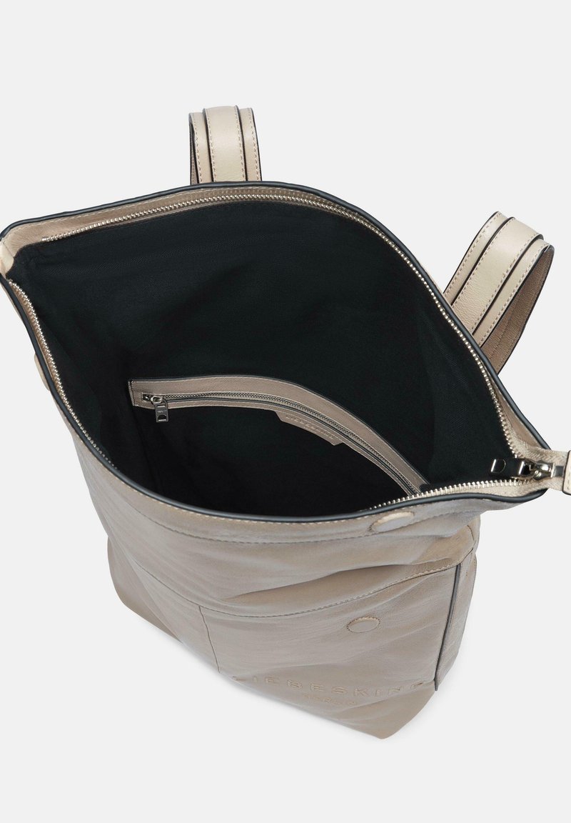 Beige Leder-Rucksack mit einem Reißverschluss-Öffnung, strukturiertem Außenmaterial, schwarer Innenauskleidung und einem Reißverschluss-Innentaschen. Zwei verstellbare Träger.