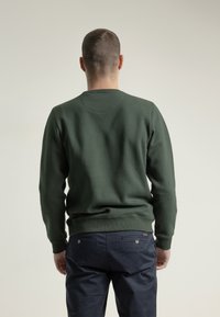Sudadera verde oscuro con cuello redondo y puños acanalados, combinada con pantalones azul marino que cuentan con bolsillos traseros y detalles de botones.
