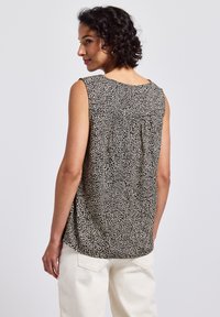 Top sin mangas en beige con estampado de leopardo negro. Presenta un escote redondeado y un corte relajado con pliegues detallados en la parte posterior.