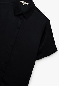 Zwarte korte mouwen shirt van gladde stof, met een knoopsluiting aan de voorkant, puntige kraag en subtiele textuur.