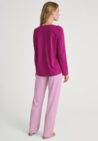 Fuchsia pyjama-top met lange mouwen, gecombineerd met roze en witte gestreepte broek. Zacht materiaal, comfortabele pasvorm, subtiele ronde halslijn, mouwen van volledige lengte.
