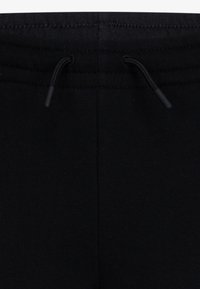 Černé tepláky s elastickým pasem a šňůrou na stažení, vyrobené z měkké látky s hladkým povrchem. Bez vzorů nebo grafik.